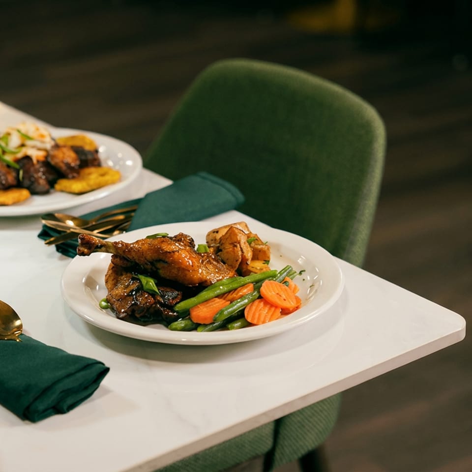 Elegant restaurant table featuring plated roasted chicken, shrimp, vegetables, and fried plantains with emerald napkins and gold flatware.